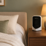 Bedside scene with a white Albus Health device on a wooden nightstand, next to a lamp and a potted plant, beside a cozy bed.
