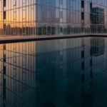 Infinity-edge rooftop pool on a tall glass building, reflecting the sunset-lit city skyline in the water.
