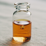 Glass vial with amber liquid standing on a textured surface.