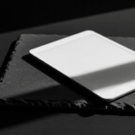White tablet resting on a textured notebook on a dark surface with dramatic shadows, angled to the right.