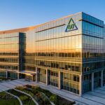 Modern glass-front office building at sunset with landscaped plaza and a triangular logo on the facade