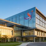 Modern glass office building with a colorful company logo on the upper corner, sunset lighting.