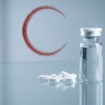 Vial of medicine with a white cap next to scattered white tablets on a reflective glass surface.