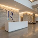 Modern office lobby with a white reception desk, stone veneer walls, and a large blue R logo.