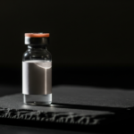 Small glass vial with orange cap on a dark textured surface and black background.